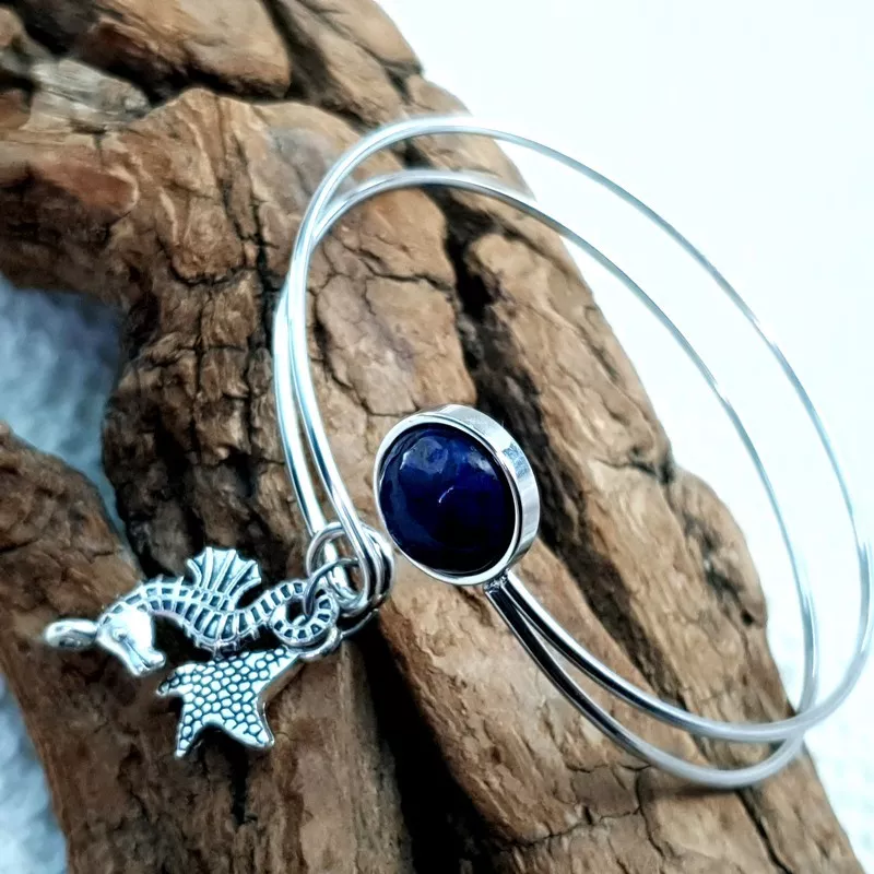 Le bracelet jonc Sylvaine est en acier inoxydable argenté, réglable, avec un cabochon en lapis-lazuli et une breloque. Le bracelet jonc Sylvaine est en acier inoxydable argenté, réglable, avec un cabochon en lapis-lazuli et une breloque.