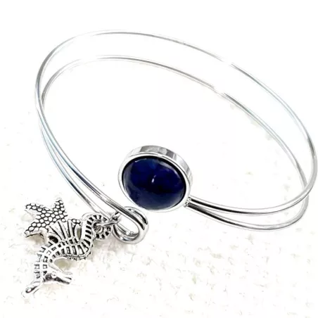 Le bracelet jonc Sylvaine est en acier inoxydable argenté, réglable, avec un cabochon en lapis-lazuli et une breloque.