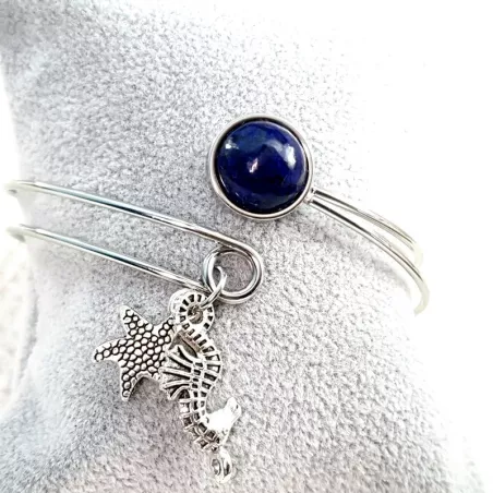 Le bracelet jonc Sylvaine est en acier inoxydable argenté, réglable, avec un cabochon en lapis-lazuli et une breloque.