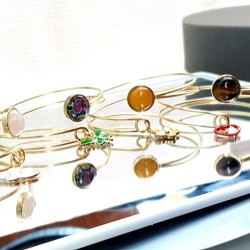 Le bracelet jonc Sylvaine est en acier inoxydable doré, réglable, avec un cabochon en verre ou pierre naturelle et une breloque.