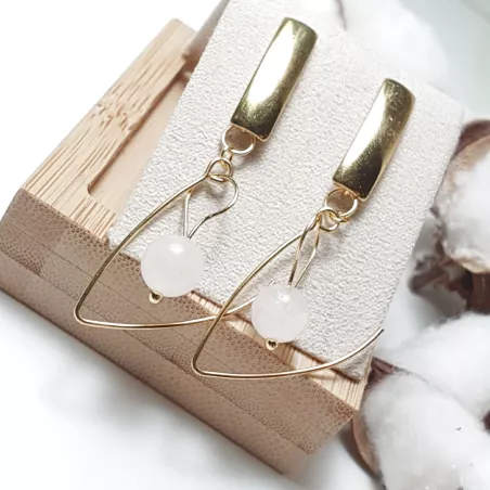 Boucles pendantes Altéra dorées avec quartz rose sur présentoir en bois